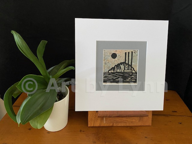 Framed relief print of the Rock in Morro Bay, next to a house plant.